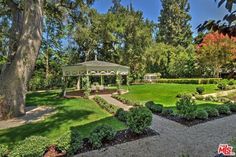 a gazebo in the middle of a lush green park with lots of trees and bushes