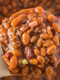 a spoon full of beans and meat on top of some kind of food that is being held by someone