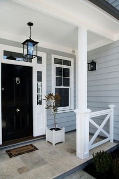 a black door and white pillars on a gray house with a potted plant next to it