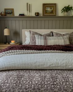 a bed with pillows and blankets on top of it next to a shelf filled with pictures