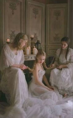 two women in white dresses sitting on a couch next to another woman with long hair