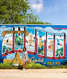 a woman standing in front of a large sign that says greetings from the capital of texas