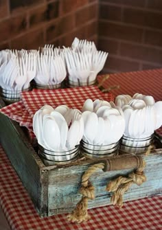 a wooden box filled with white utensils on top of a red and white checkered table cloth