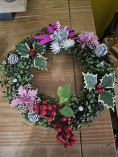 a christmas wreath with holly, berries and pine cones on a wooden table in the process of being made