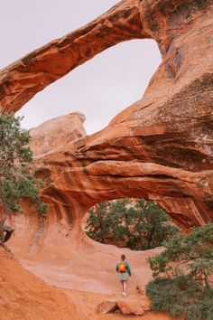 a person standing in the middle of a desert area with an arch shaped rock formation