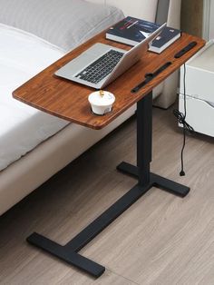 a laptop computer sitting on top of a wooden desk next to a bed with white sheets