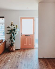 an orange door is in the middle of a white room with wood floors and a brown leather couch