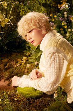 a woman sitting on the ground in front of some plants and flowers wearing a sweater