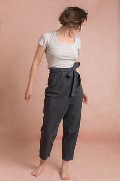 a woman standing in front of a pink background wearing black pants and a white t - shirt