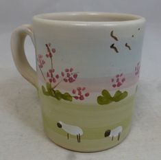 a ceramic mug with sheep and flowers painted on it's side, sitting on a table