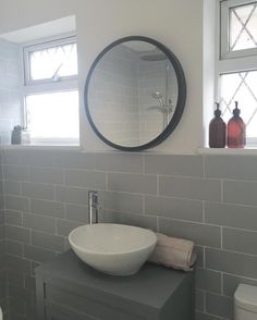 a white sink sitting under a round mirror in a bathroom next to a toilet and window