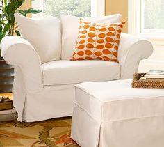 a white chair and ottoman with orange pillows in a living room next to a potted plant