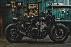 a black motorcycle parked in front of a green wall with shelves on it and other items