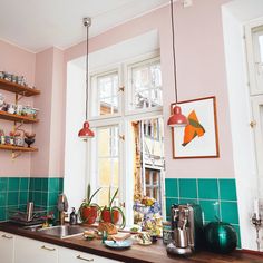 a kitchen with pink walls and green tile on the counter top, along with potted plants