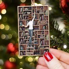 a person holding up a book shelf ornament in front of a christmas tree