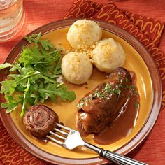 a yellow plate topped with meat and potatoes next to green vegetables on top of a red table cloth