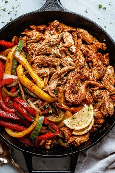 a skillet filled with chicken, peppers and lemons on top of a table