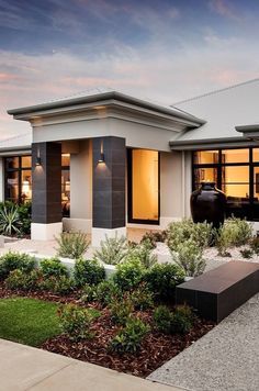 a modern house is shown at dusk with the lights on and plants in the front yard