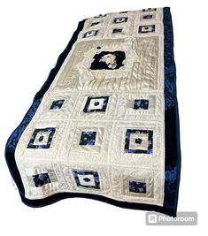 a white and blue quilted blanket with black squares on the bottom, along with an applique design