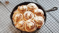 a skillet filled with cinnamon rolls sitting on top of a metal table next to a wire rack