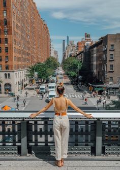 a woman standing on the edge of a bridge looking down at a cityscape