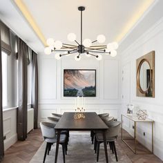 an elegant dining room with white walls and wood flooring is lit by a modern chandelier