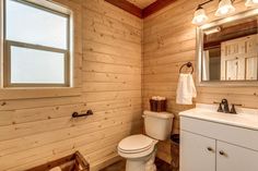 a white toilet sitting next to a sink in a bathroom under a wooden ceiling mounted mirror