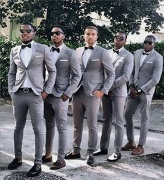 a group of men standing next to each other wearing suits and bow ties on the street