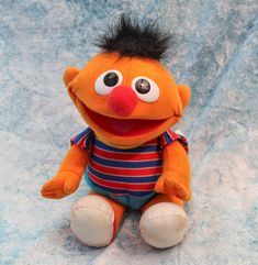 an orange stuffed animal with black hair sitting on a blue sheeted surface and looking at the camera