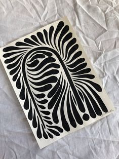 a piece of paper with black and white designs on it sitting on a bed sheet