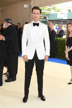 a man in a tuxedo and bow tie standing on a white carpet at an event