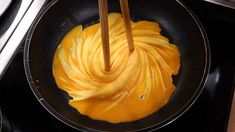 two wooden chopsticks in a frying pan filled with yellow food on the stove