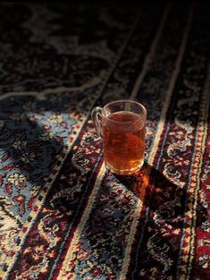 a cup of tea sitting on top of a rug next to a light shining through the window