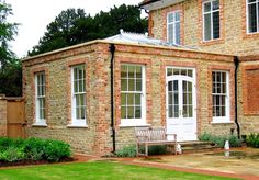 a brick house with white doors and windows on the front lawn, surrounded by greenery