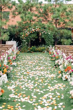 an outdoor ceremony with flowers on the grass and petals in the aisle leading up to it