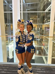 two cheerleaders posing for the camera in front of a large glass window with their arms around each other