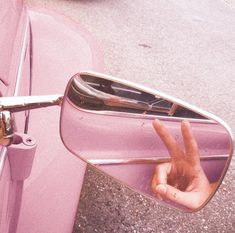 a person's hand sticking out the side mirror of a pink car