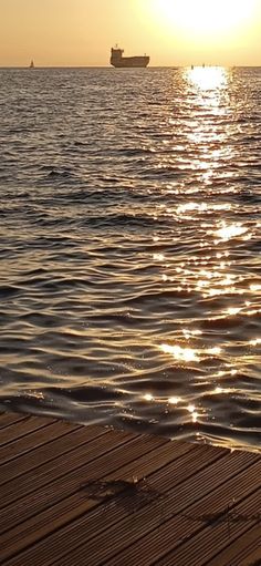 the sun is setting over the ocean with a boat in the water and a dock