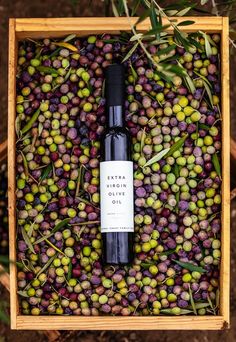 a bottle of extra virgin olive oil in a wooden box filled with green and purple olives