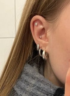 a close up of a person with ear piercings on their ears and behind them is a white tile wall