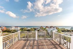 a wooden deck with white railings overlooks the ocean and houses in the distance