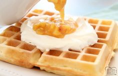 a waffle being drizzled with syrup and whipped cream