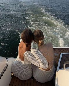 two women sitting on the back of a boat looking out at the water and land