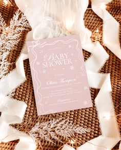 a pink baby shower card sitting on top of some white streamers and ribbon with snowflakes around it