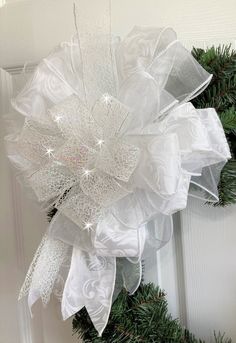 a white christmas wreath hanging on the front door with ribbon and sequined bow