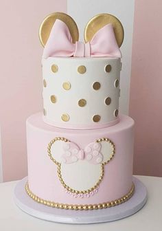 a pink and white cake with minnie mouse ears on it's top is decorated with gold polka dots