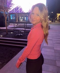 a woman is standing on the sidewalk in front of a building and smiling at the camera