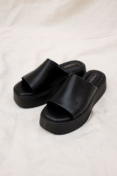 Vagabond Shoemakers Courtney platform slides. It is all about the characteristic flared outsole that makes this pool slide style the ultimate sandal of the season. The simple slip-on upper, made from black leather, is grounded by tonal flatform soles measuring 50 mm. Details include padded insoles and square toes. Heel height 50mm. Cow leather upper, Pu outsole, textile lining, cow leather inner sole. This style is made by Gia Ding Shoes Co. Ho Chi Minh City, Vietnam. 5134-001-92 / 5334-601-92 P