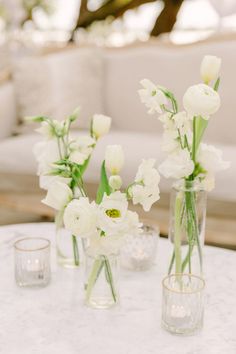 white flowers in vases sitting on a table next to two glasses and a couch