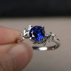 a person holding a ring with a blue stone in it's center and leaves around the band